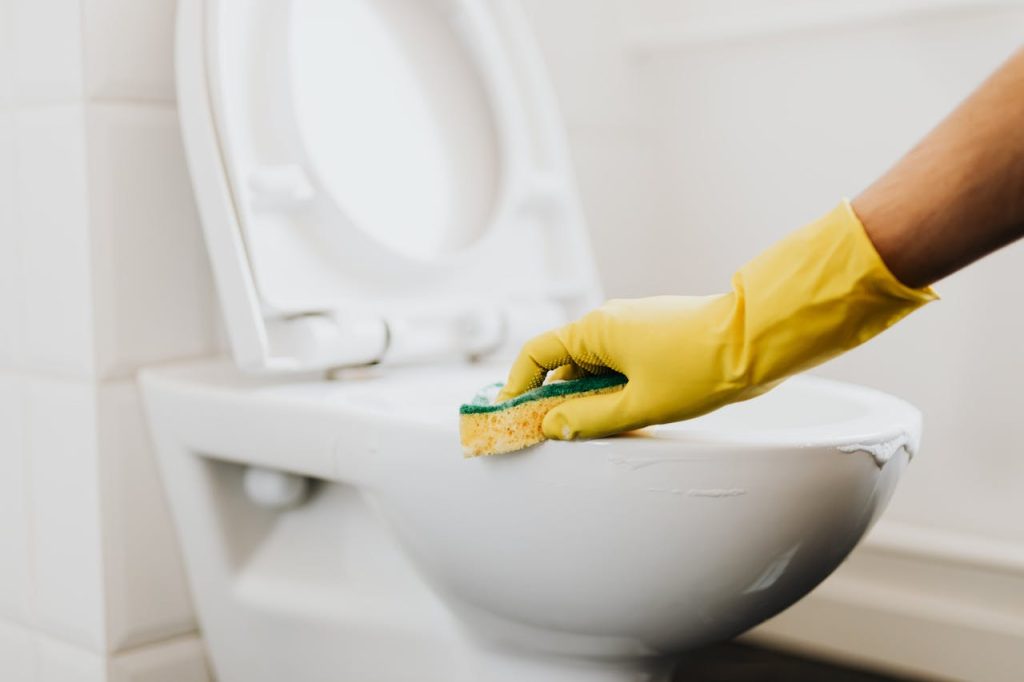 pexels-photo-4239071 A close-up of a hand in a yellow glove cleaning a toilet with a sponge, promoting hygiene.